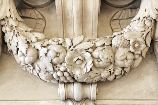 Beautiful detailed carving of a garland with leaves, flowers and fruits part of the marble stone mantle of a luxurious fireplace.