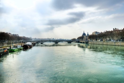 Beautiful scenery of a misty morning over the Rhone river in Lyon France with a bridge and old european architecture and barges or houseboats over the green waters, HDR rendering.
