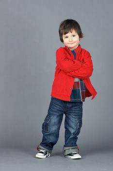 Super cute young or little boy smiling dressed in cool red corduroy shirt and jeans, leaning on one side, shot in studio  over grey background.