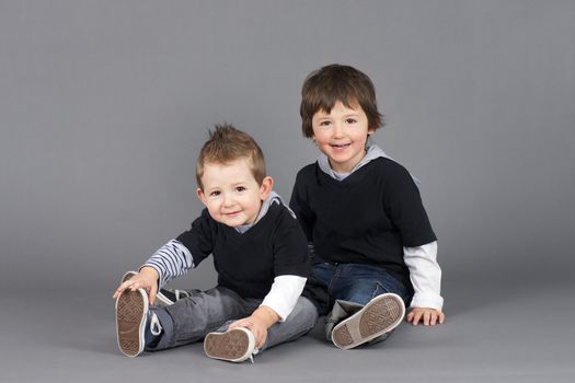 So cute, two little hip and cool young little boys, brothers, shot in studio over grey background.