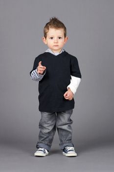 Cute and hip little toddler boy pointing at camera with a serious look on his face over grey background with white speech bubble easy to remove.