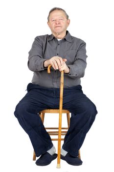 Senior or old man sitting down on old wooden chair with his cane to rest, wearing blue corduroy and slippers, isolated on white.