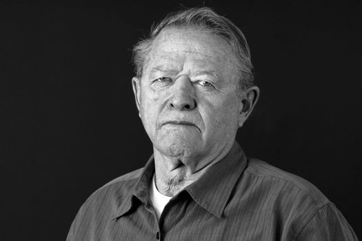 Dramatic black and white portrait of a senior man looking very serious, sad or depressed looking at camera,great facial details, shot in studio over black.