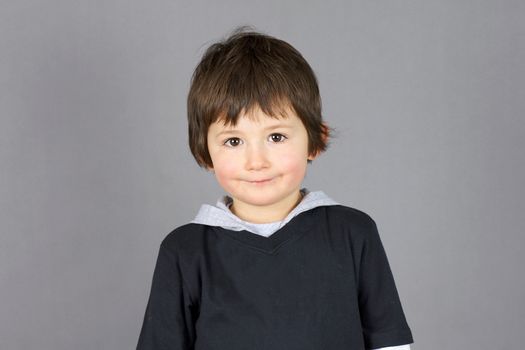 Super cute little boy preschooler with big brown eyes and a charming hint of a smile over grey background.