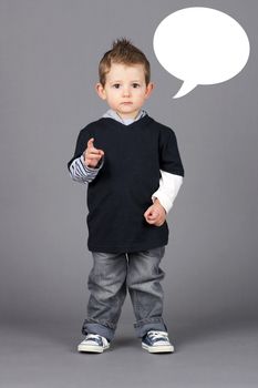 Cute and hip little toddler boy pointing at camera with a serious look on his face over grey background with white speech bubble easy to remove.