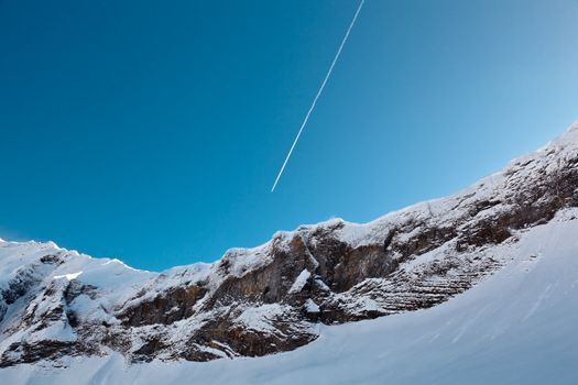 Airplane Trail in Blue Sky above Mountain Peak, French Alps
