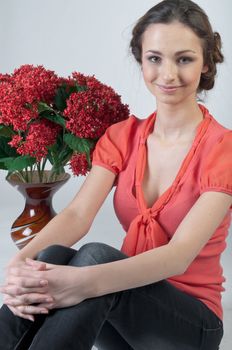Portrait of a young beautiful girl with a bouquet of red flowers in vase