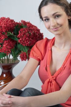 Portrait of a young beautiful girl with a bouquet of red flowers in vase