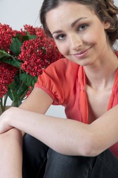 Portrait of a young beautiful girl with a bouquet of red flowers in vase
