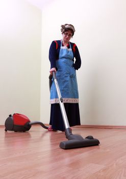 Housewife using a vacuum cleaner to clean the floor. The mai focus is on the tube of the cleaner.