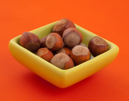 Group of hazelnuts in a bowl, with orange background and copy space.