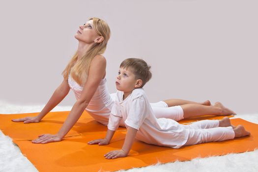 A beautiful young mother practices yoga with her son