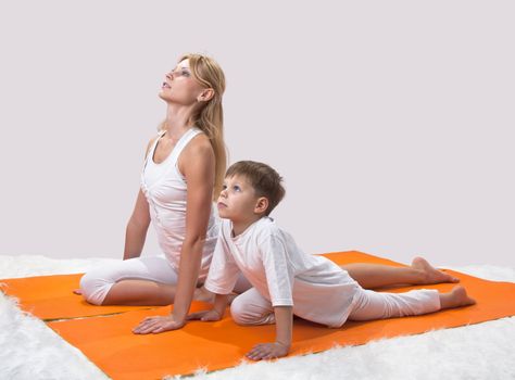 A beautiful young mother practices yoga with her son 