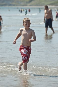 an image of a young boy wearing boardshorts running through the water on a hot summers day