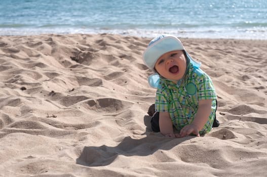 Happy baby boy on the beach sitting in sand