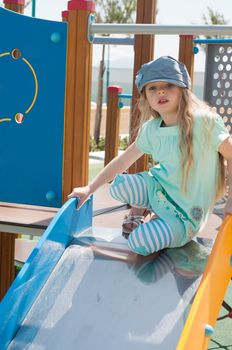 Little girl with long hair denim peaky cap playing in playground