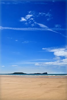 white fluffy clouds and blue skies over empty sandy beach, gower wales