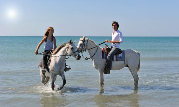 father and daughter with arabian and camargue horses in the sea with an evening sun