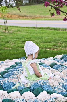 Amish child sitting on an old biscuit quilt.