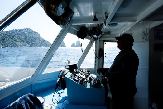 fat scilhouetted man steering ship, with sea and craggy coast behind