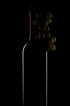 bottle of wine and a bunch of grapes on a black background