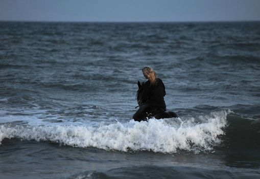 young woman an her black stallion swimming in the sea at night