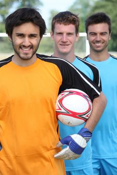 Three smiling footballers with ball