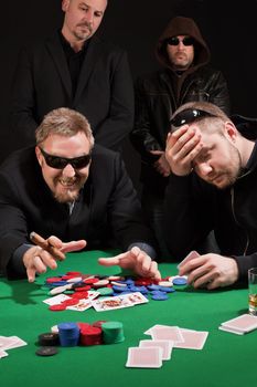 Photo of two male poker players, one winning and the other losing, while security watches over their shoulders. Cards have been altered to be generic.