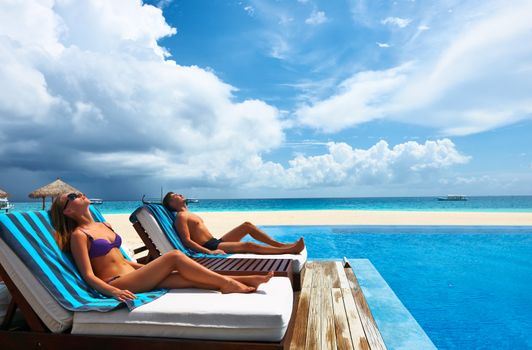 Couple relaxing in chaise lounge at the poolside 