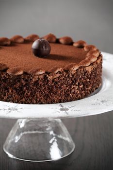 Photo of a delicious chocolate cake with truffle on top. Cake is on a plate with icing sugar with snowflake accents. Focus is on the front edge.