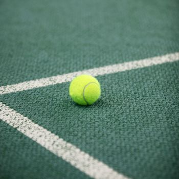 Luminous green high visibility tennis ball on a green tennis court lying in the angle of the lines forming the corner