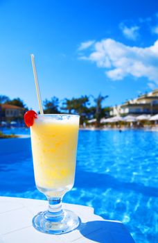 cocktail in glass with a cherry on a background blue water of pool