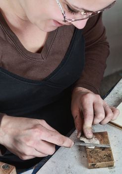 Close-up image of a female jeweler filing a piece of metal in her workshop.