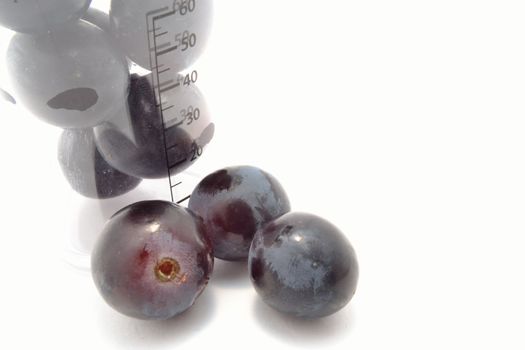 The black grape berries and measuring glass over white
