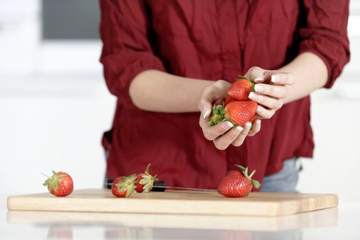 Beautiful young woman preparing strawberries in her white kitchen