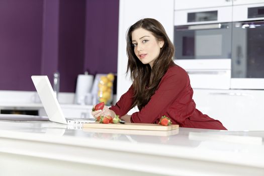 Beautiful young woman reading a recipe from a laptop in her kitchen