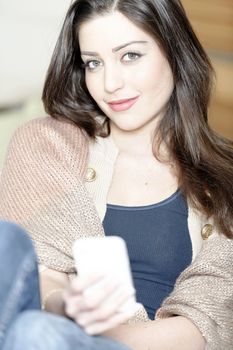 Beautiful young woman chatting on her mobile phone in her kitchen