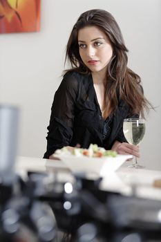 Beautiful young woman enjoying a glass of wine in her kitchen, while preparing food.