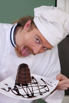 Funny young chef eating a piece of cake with chocolate sauce 