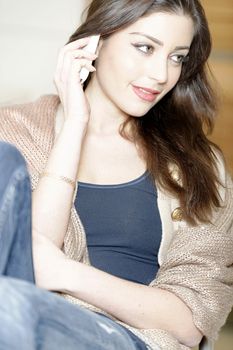 Beautiful young woman chatting on her mobile phone in her kitchen