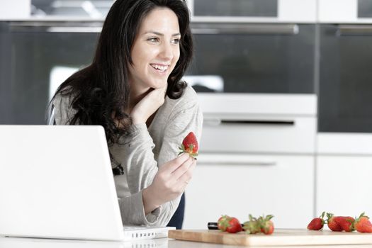 Beautiful young woman reading a recipe from a laptop in her kitchen