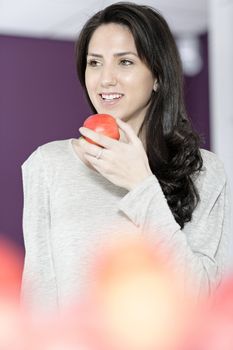 Beautiful young woman eating an apple in her white kitchen relaxing