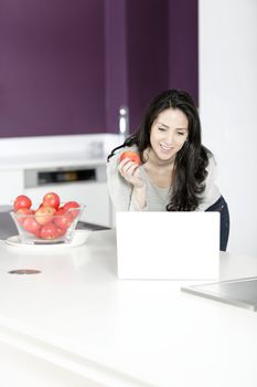 Beautiful young woman eating an apple in her white kitchen relaxing