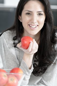 Beautiful young woman eating an apple in her white kitchen relaxing