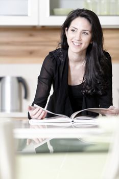 Beautiful young woman reading from a recipe book in her kitchen