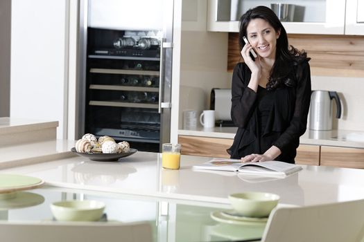 Attractive young woman talking on the phone in her kitchen