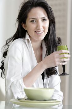 Beautiful young woman sat at the dinner table drinking a glass of wine.