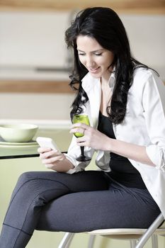 Beautiful young woman chatting on her mobile phone in her kitchen