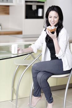 Beautiful young woman taking a break in her kitchen with a coffee and cake.