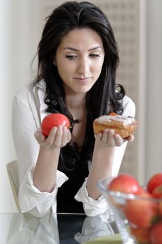 Attractive young woman choosing between a sticky cake or fresh fruit.